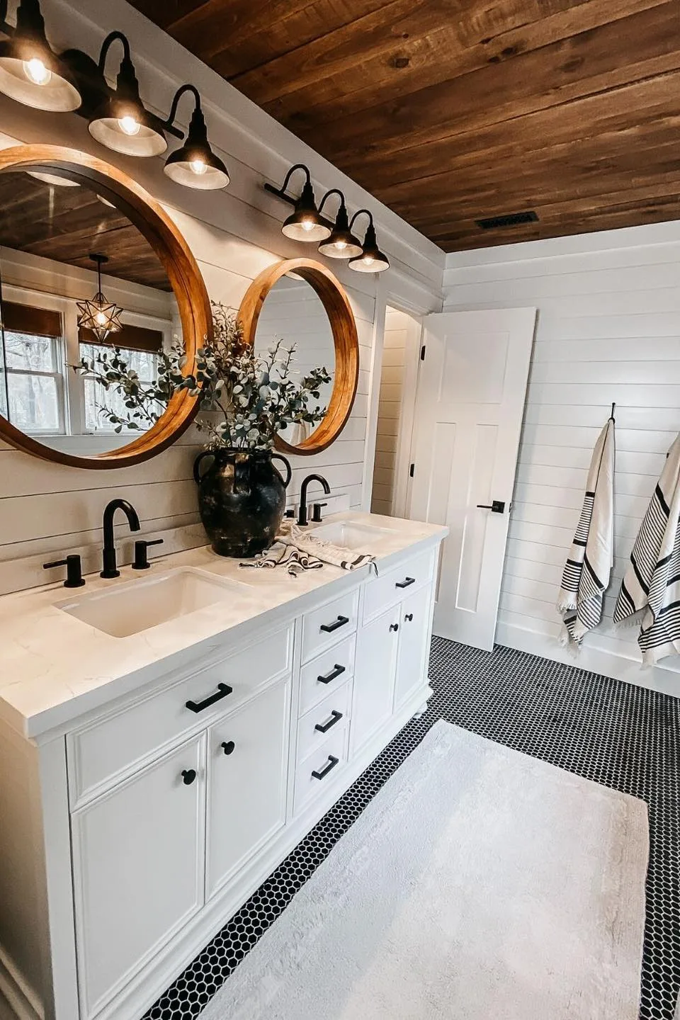 White bathroom remodel with wood ceiling, round mirrors, and black hardware